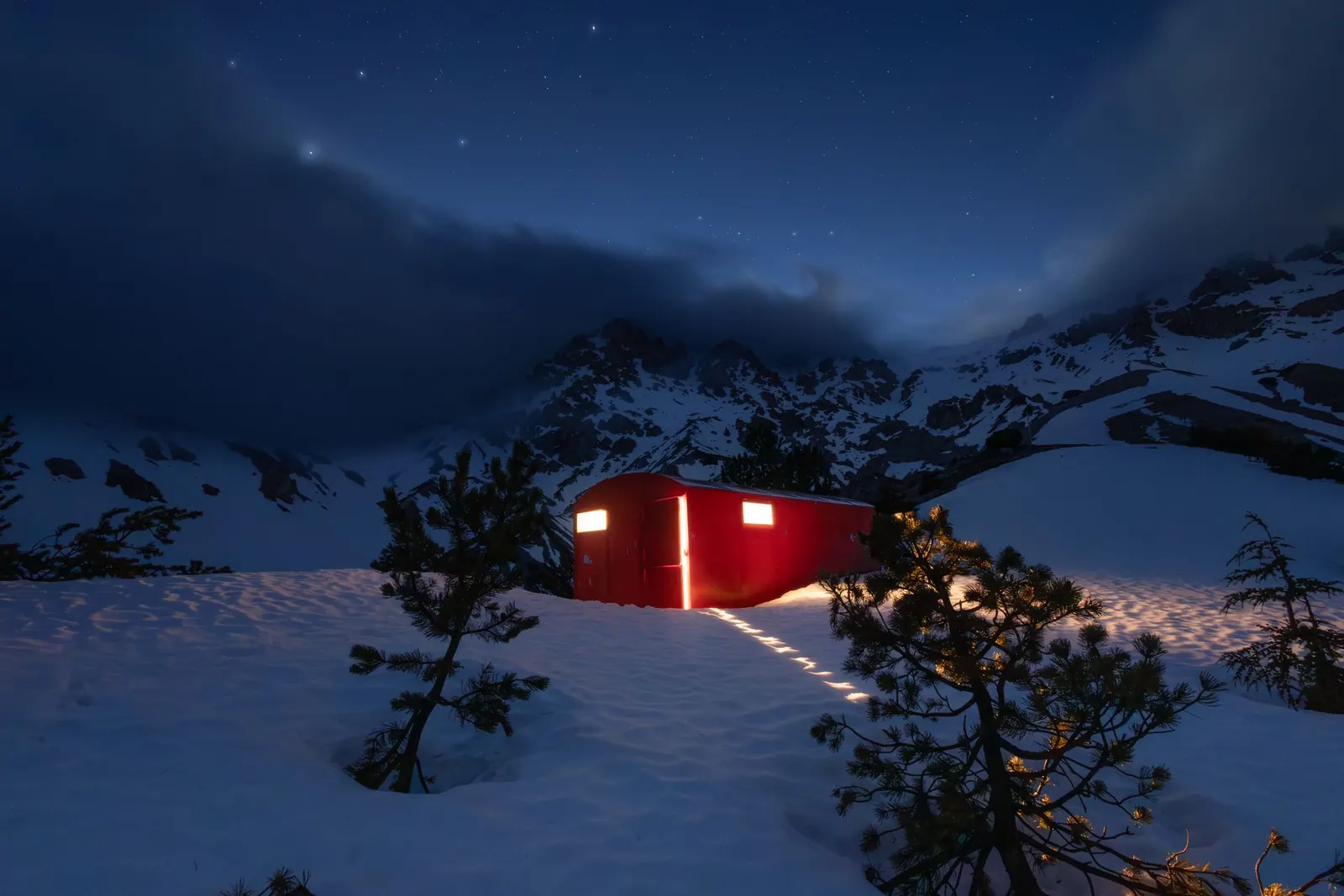 A red cabin glowing under a starry mountain sky
