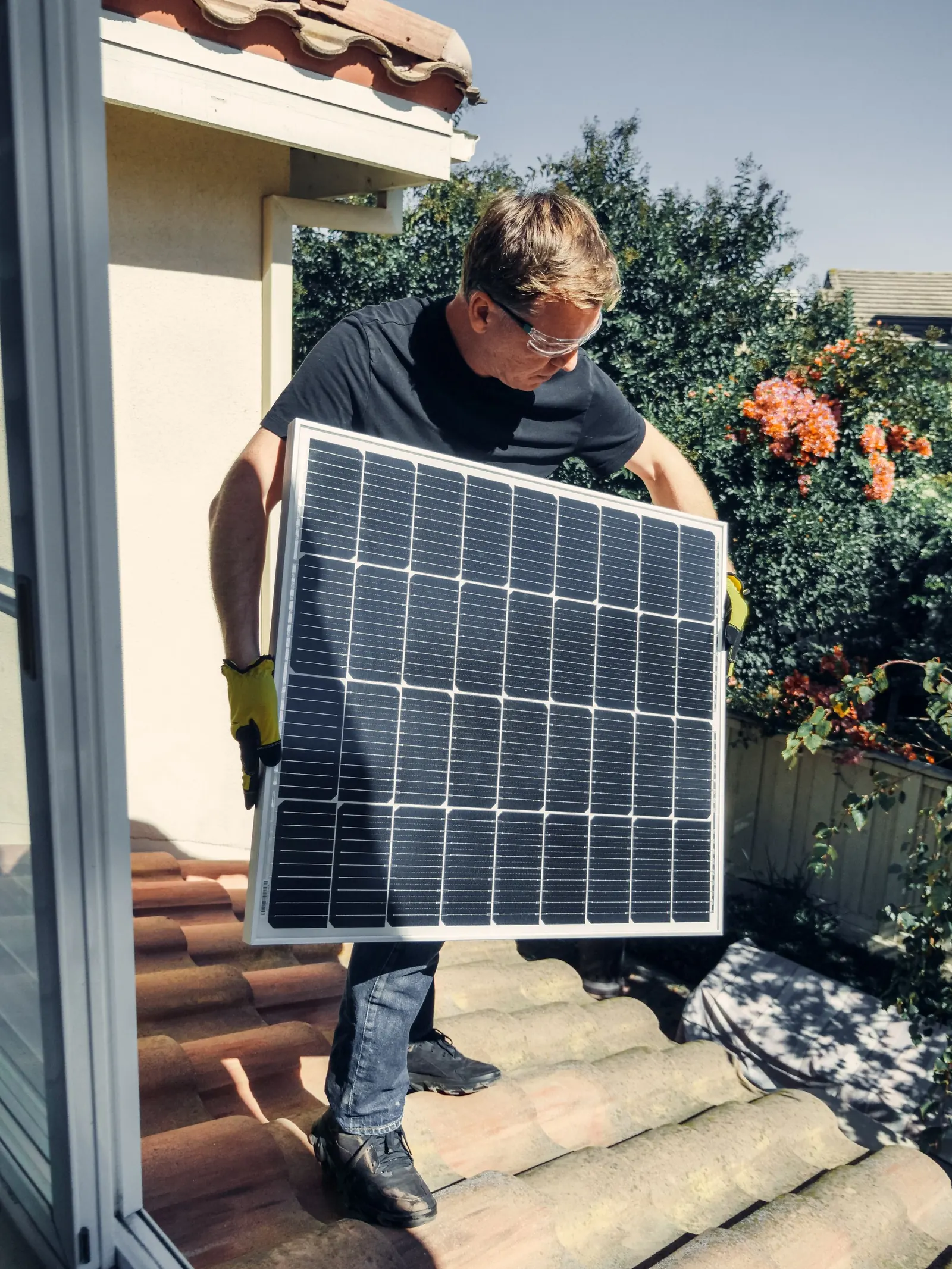 A technician carrying a solar panel on a roof